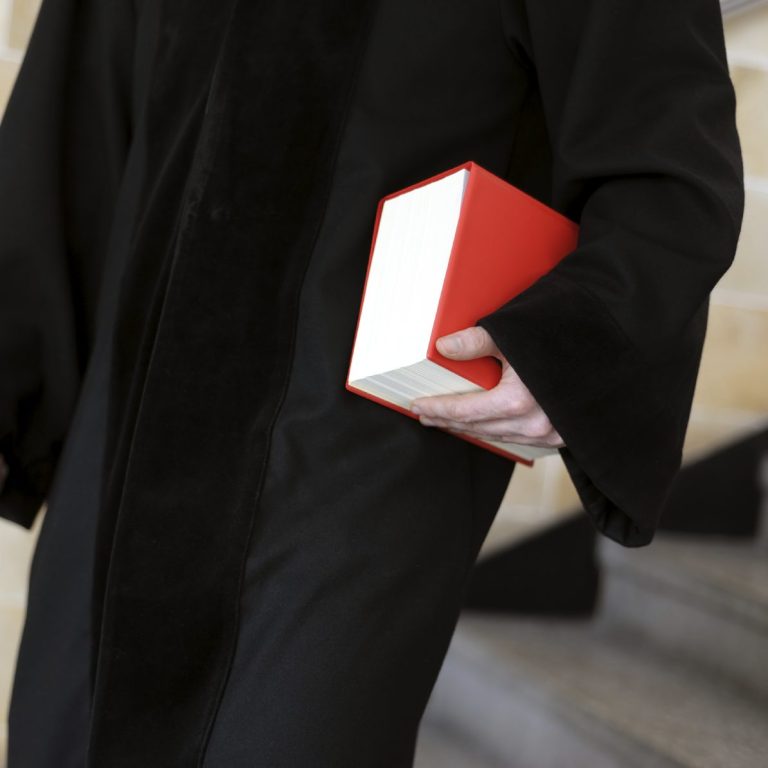 Rechtsanwalt in schwarzem Gewand hält ein roter Gesetzessammlung.